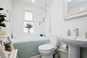 A bathroom with a toilet, sink, shower, and a window with a flower vase.