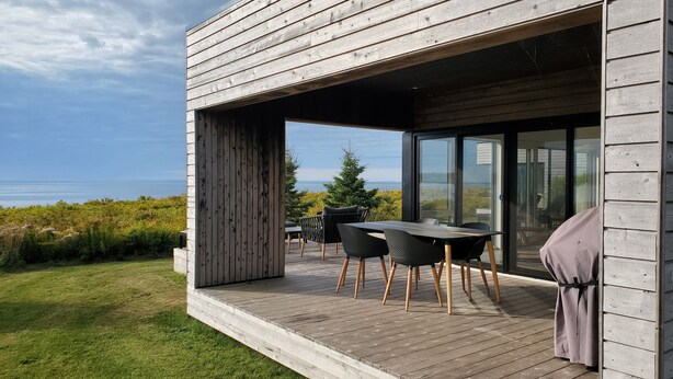 Et moderne hus med en træterrasse, et bord med stole og en glasdør til en patio.