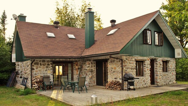 Ein Steinhaus mit einer Holzdielen-Terrasse, einem Grill und Sitzgelegenheiten im Freien.