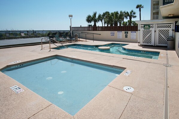 A swimming pool area with multiple pools, a lifeguard stand, and a fenced deck with lounge chairs. - Luxury oceanfront resort-workout room, indoor/outdoor pools, lazy river, kids' pool-in Ocean Drive (North Myrtle Beach)