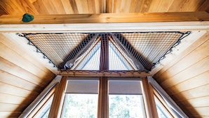 Una cabaña de madera con techo inclinado, ventana con cortinas y cielo cubierto de mosquitera.