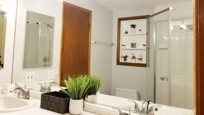 Een badkamer met een grote spiegel, twee wasbakken, een douche en een plank met toiletartikelen.