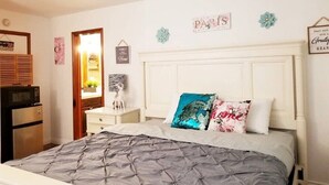 Een slaapkamer met een bed, een dressoir, een magnetron en een koelkast.