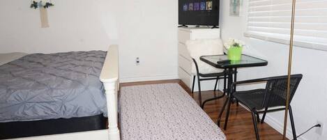 Una habitación pequeña y ordenada con cama, escritorio, silla y televisor.