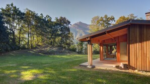 A modern wooden cabin with a glass door entrance, surrounded by a grassy area and trees. - Architect's house not overlooked in the Ossau valley, spa & sauna, 7000m2 park (Béost)