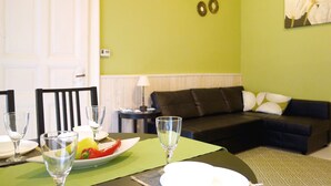 A dining area with a table set for two, a green wall with decorative metal pieces, a black sofa, and a painting of flowers.