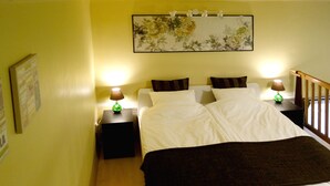 A hotel room with a bed, two nightstands, a green lamp, and a painting on the wall.
