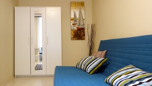 A bedroom with a blue bed, striped pillows, a white wardrobe, and a painting of sailboats.