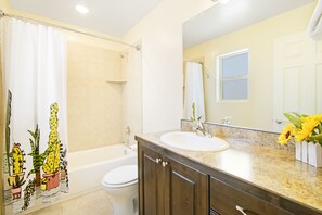 Een badkamer met douchegordijn, bad, toilet, wastafel en spiegel.