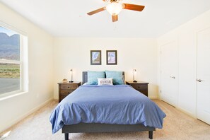 Een slaapkamer met een bed, twee nachtkastjes, een plafondventilator, een raam met uitzicht en een deur.