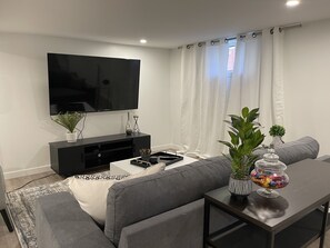 A modern living room with a flat-screen TV, grey sofas, a coffee table, and a small plant on a side table.