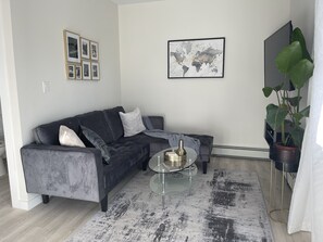 A modern living room with a grey sectional sofa, a glass coffee table, a world map artwork, and a large potted plant.