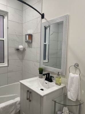 A modern bathroom with a white sink, a glass shelf, a mirror with a textured frame, a towel ring, and a potted plant.