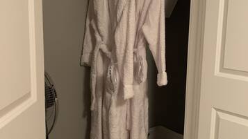A closet with a white robe hanging on a rod, a white storage bin, and a white fan against the wall.