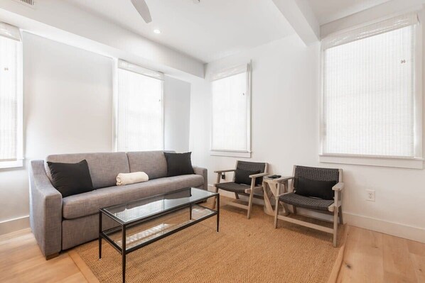 Een moderne woonkamer met een grijze bank, een glazen salontafel en twee rieten stoelen.