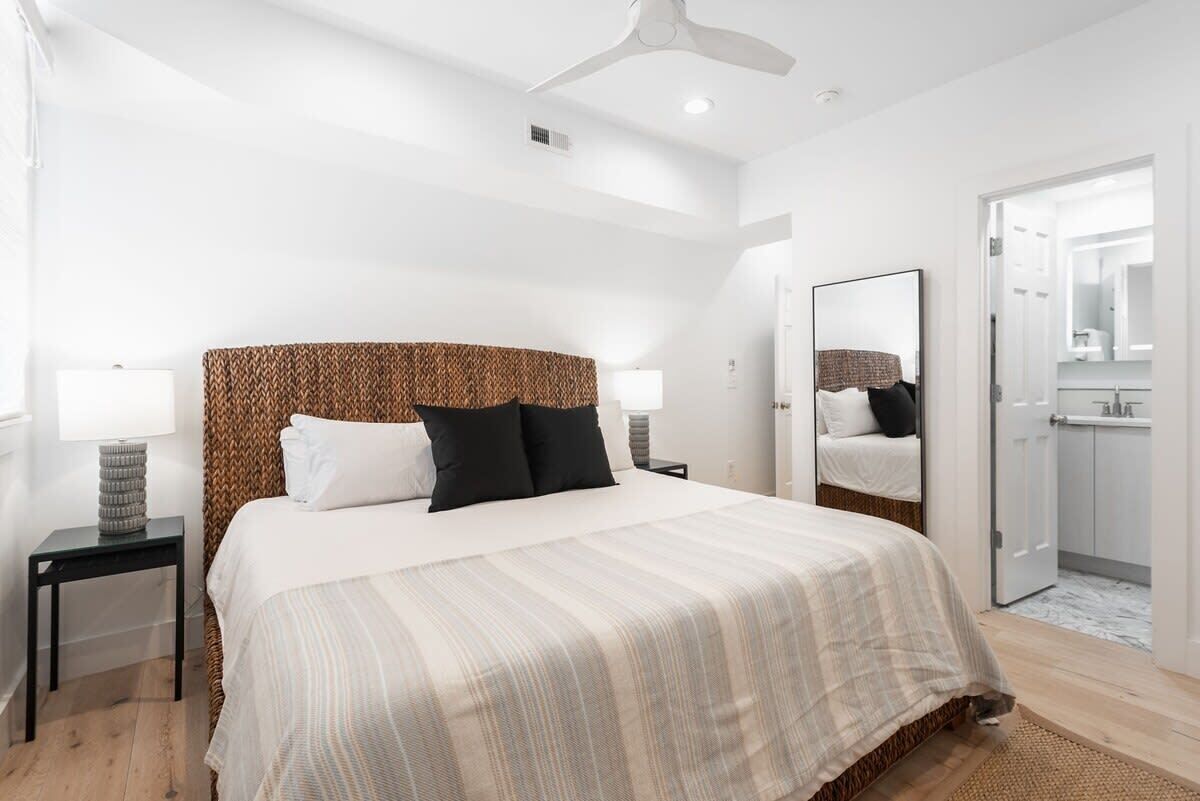 Een moderne slaapkamer met een groot bed, een plafondventilator en een zichtbare badkamer door een geopende deur.