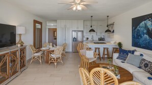 A modern kitchen with white cabinets, a refrigerator, and a dining area with wicker furniture. - Oceanfront Condo, King Bed, Pool | Unit 110 (Cabarete)