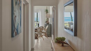 A hallway with a dining area, wicker chairs, a table, a lamp, and a view of the ocean. - Oceanfront Condo, King Bed, Pool | Unit 110 (Cabarete)