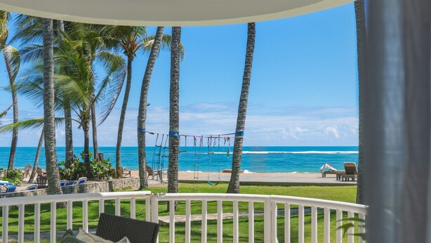 A balcony with a view of the ocean, palm trees, and beach chairs. - Oceanfront Condo, King Bed, Pool | Unit 110 (Cabarete)