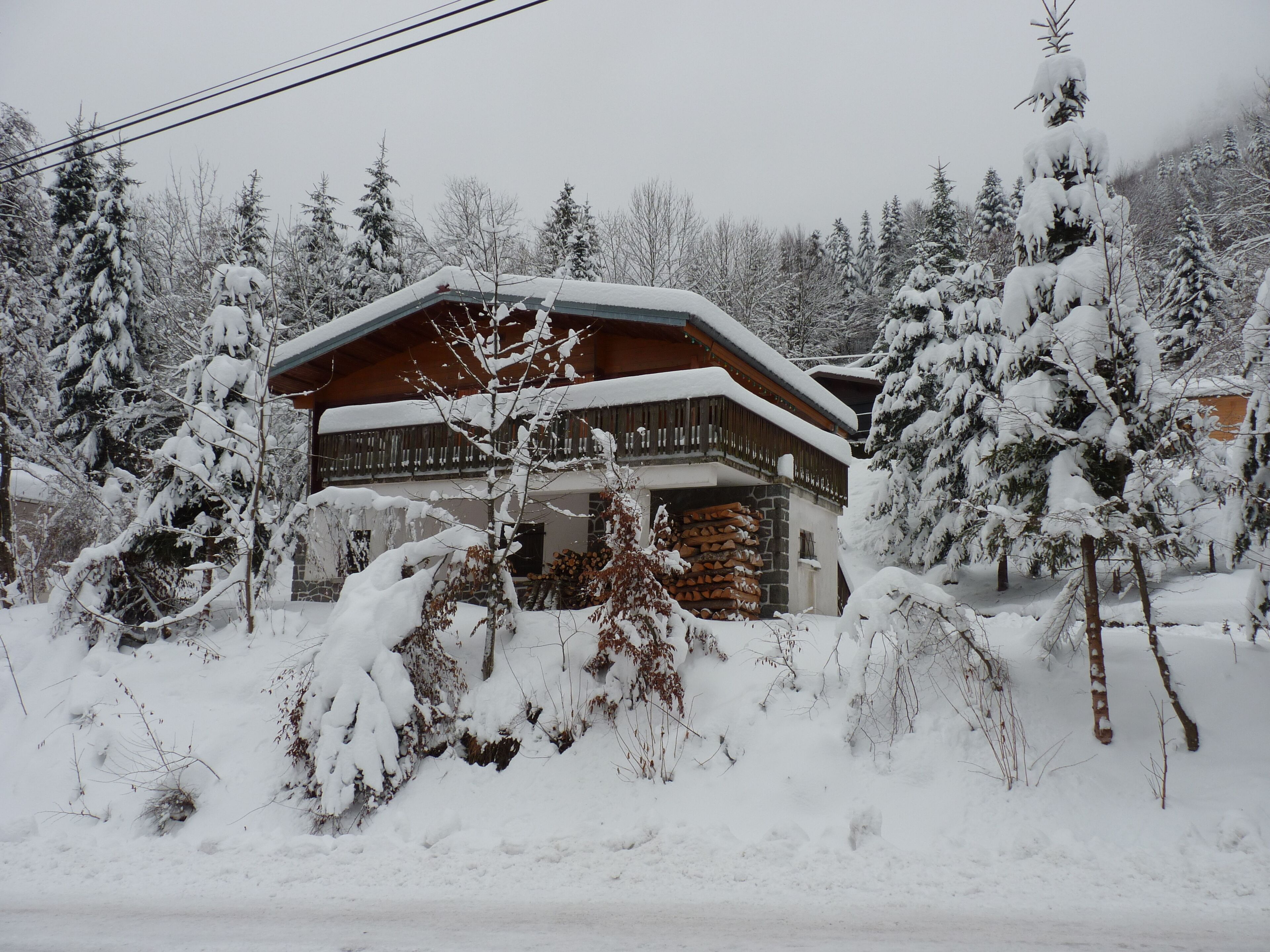 Une cabane en rondins, avec des fondations en pierre et une structure supérieure en bois, entourée d’arbres couverts de neige.
