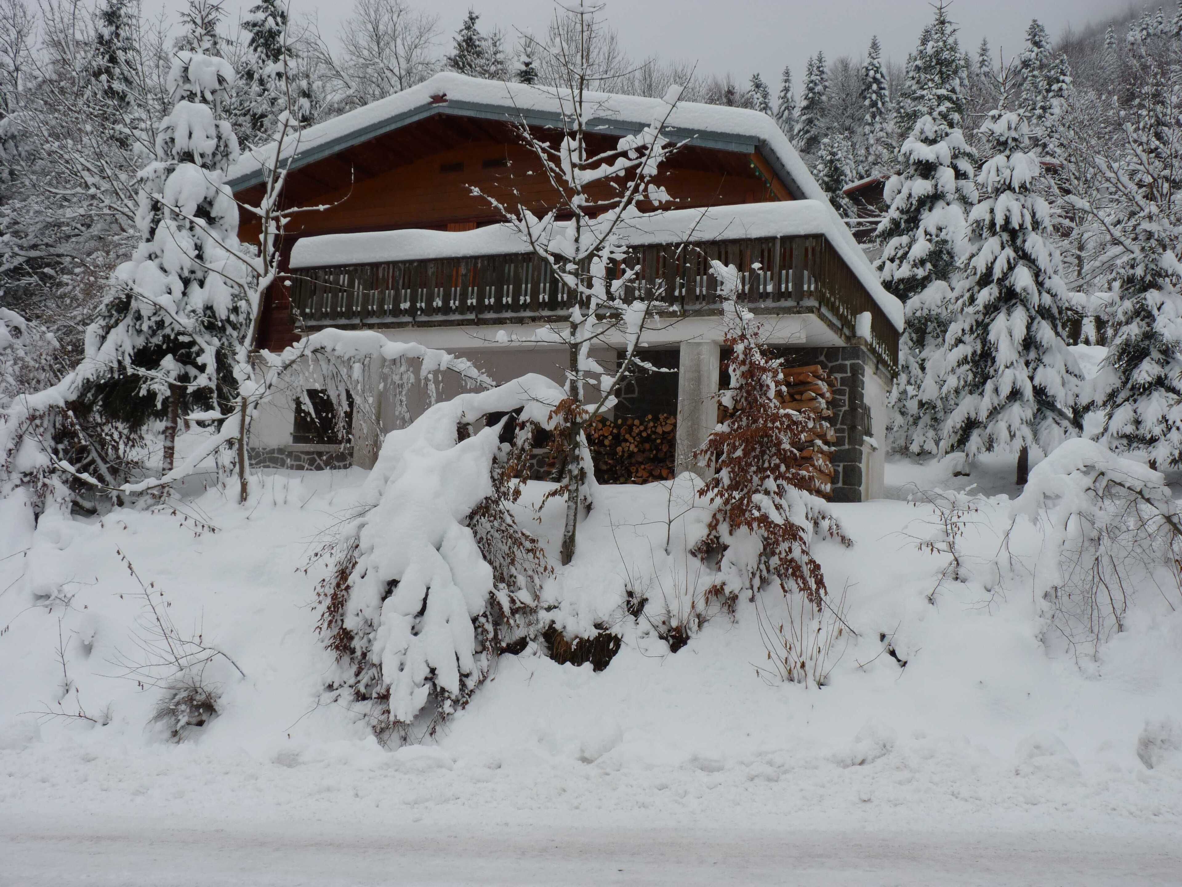 Puinen mökki, jossa on kalteva katto, ja sen ympärillä on lumipeitteisiä puita ja kivimuuri.