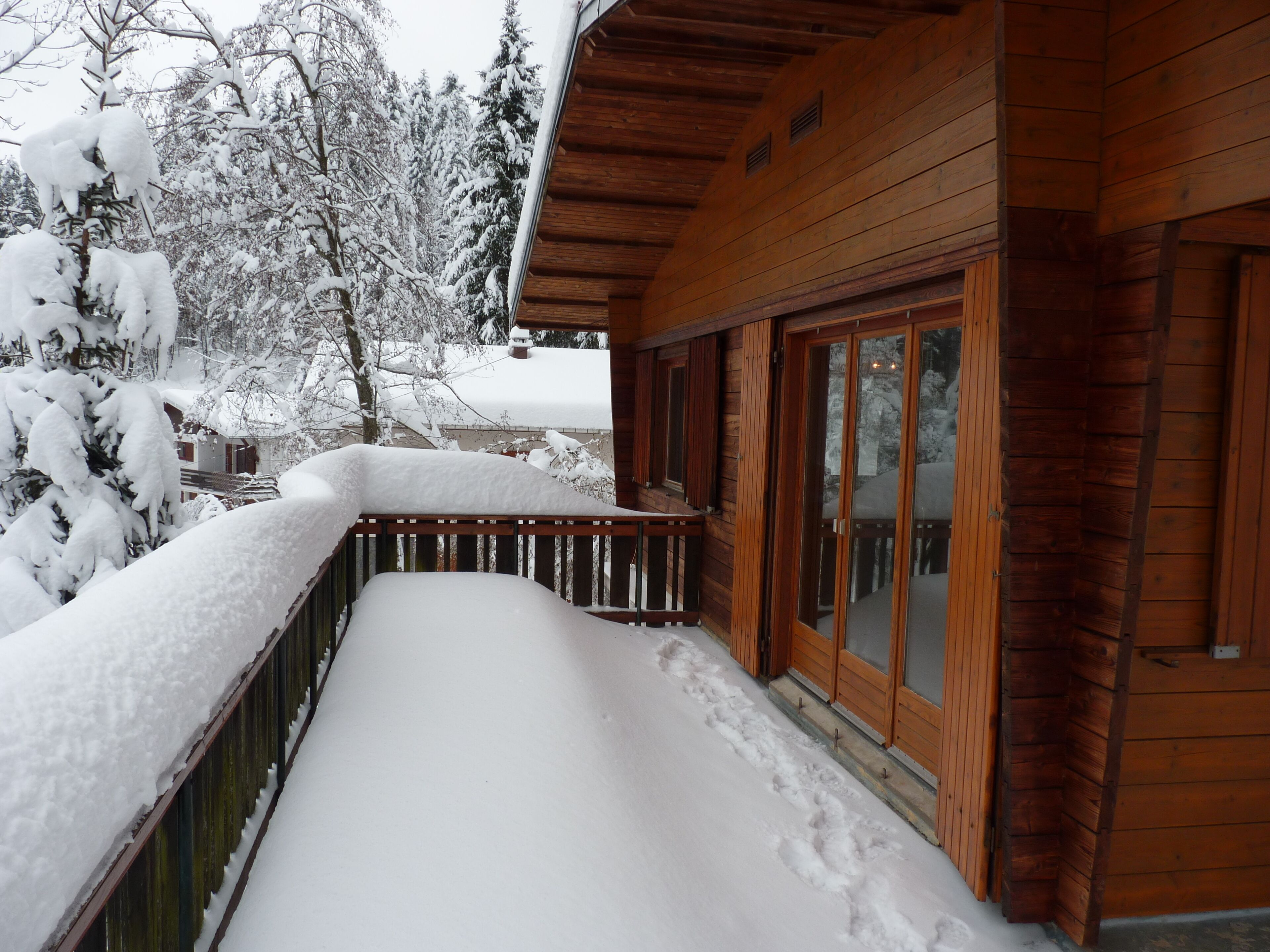 Une cabane en bois dotée d’une terrasse recouverte de neige et d’une porte vitrée donnant sur un balcon.