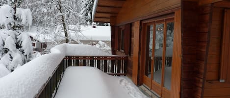 Una cabaña de madera con una terraza cubierta de nieve y un cristal que da a un balcón.