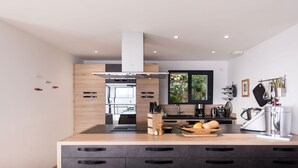 A modern kitchen with a central island, wooden cabinets, and a large window. - La détente 3149 villa (Les Issambres)