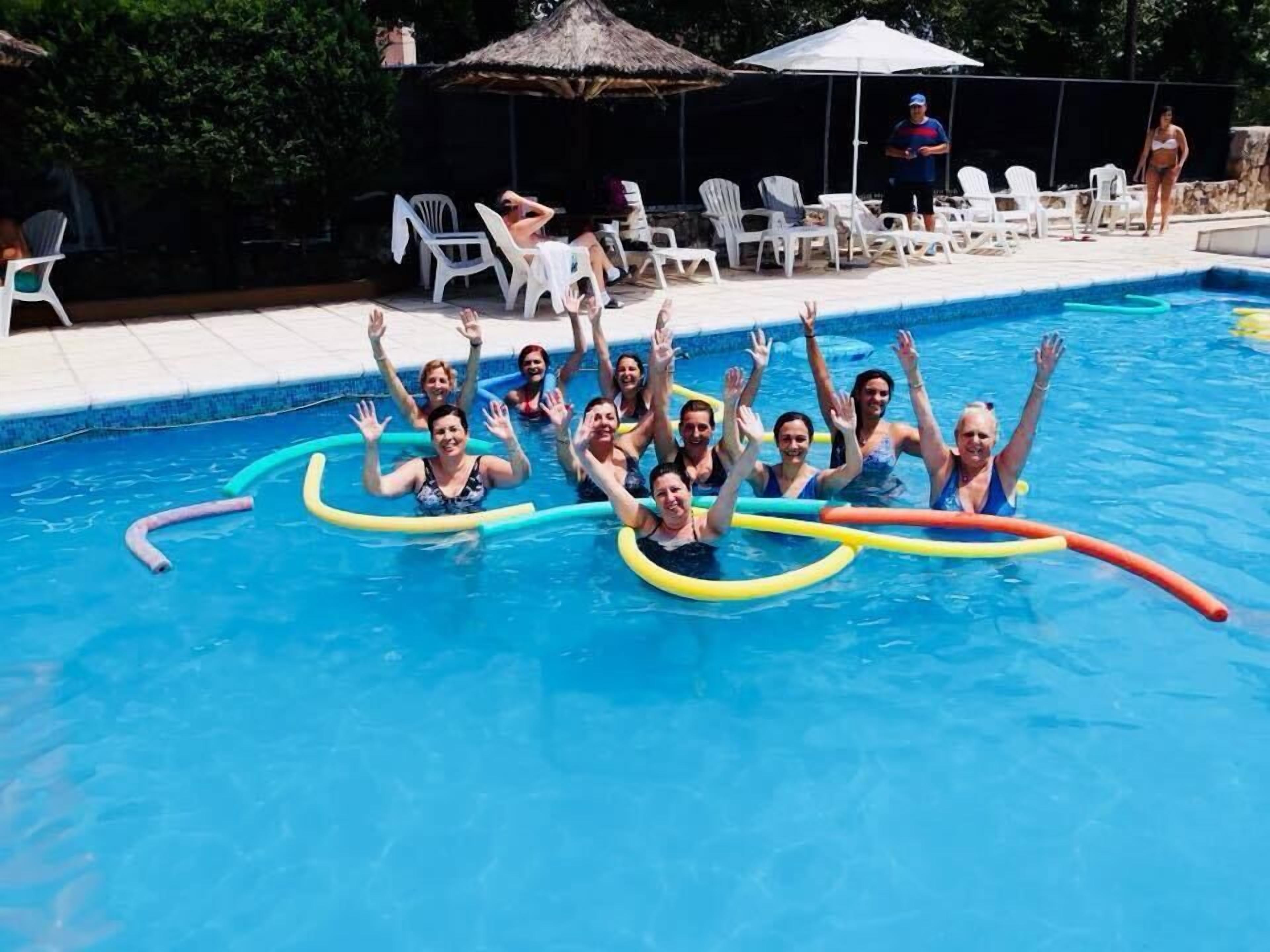 Un grupo de personas en una piscina con sillones de descanso y sombrillas al fondo.