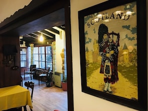 A room with a framed picture of a person in traditional Scottish attire, a table with a yellow tablecloth, and a chair.