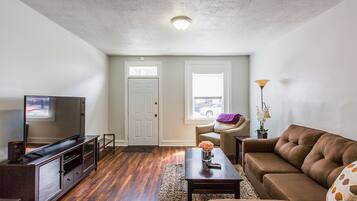 A living room with a TV, sofa, coffee table, and a door leading to another room.