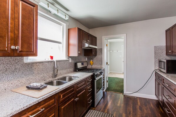A kitchen with granite countertops, stainless steel appliances, wooden cabinets, and a window providing natural light.