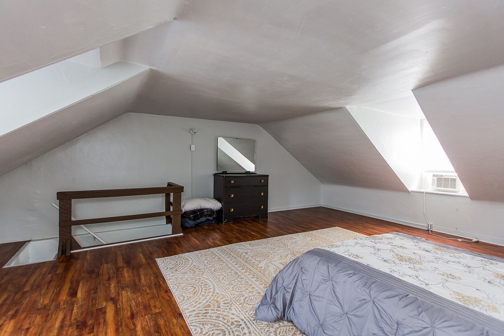 Een slaapkamer met een schuine balkenlaag, een bed, een kapstok, een spiegel en een houten bankje.