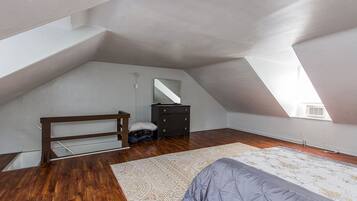 Een slaapkamer met een schuine balkenlaag, een bed, een kapstok, een spiegel en een houten bankje.
