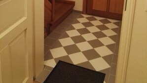 Un couloir avec un sol à carreaux, une porte en bois et un escalier.