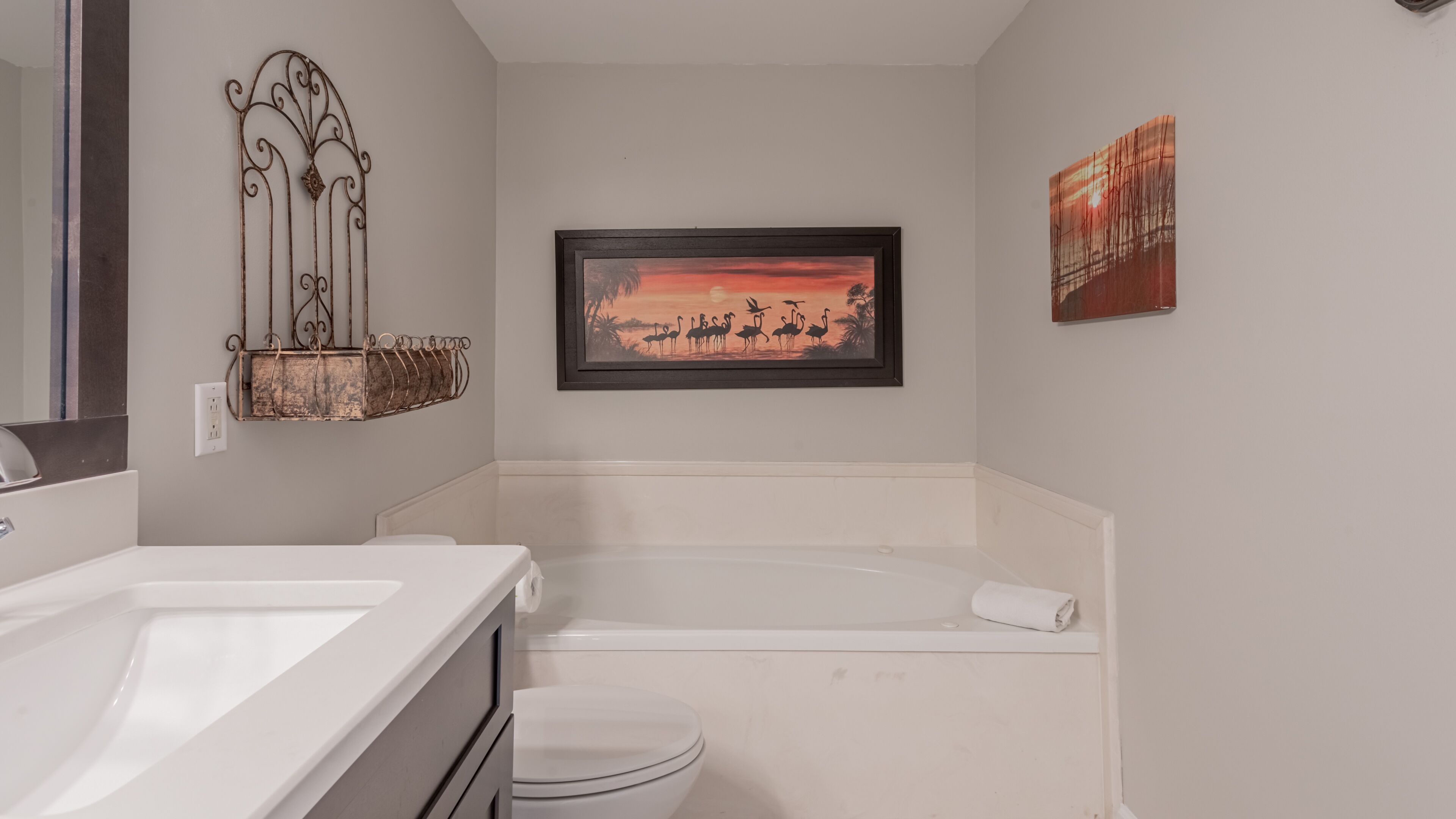 A bathroom with a white sink, a toilet, and a bathtub. There is a framed picture of flamingos on the wall.