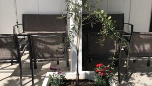 A garden area with a planter box containing a small tree and flowers, surrounded by outdoor seating. - Mia Patria apartment (Doni Štoj)