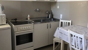 A compact kitchen with a stove, oven, sink, and a table with a tablecloth. - Mia Patria apartment (Doni Štoj)