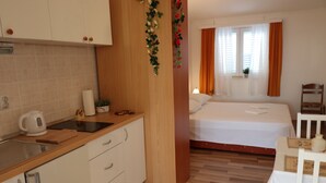Ein kleines Hotelzimmer mit Küchenzeile, einem Bett, einem Tisch und einem Stuhl.