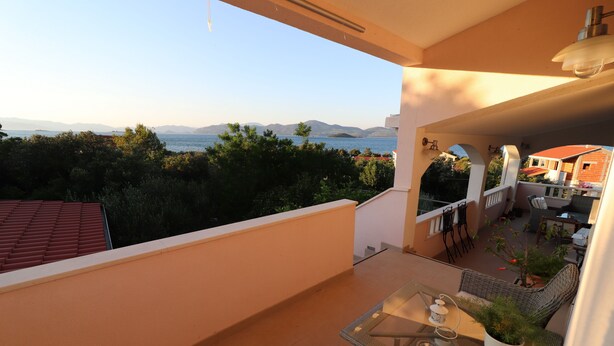 Ein Balkon mit Tisch und Stühlen, einer Topfpflanze und Blick auf das Meer und die Berge.