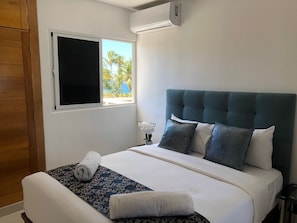 A neatly made bed with a dark patterned bedspread, a white pillow, and a rolled white towel.