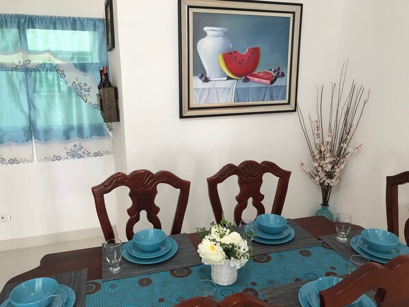 A dining table set with blue plates and bowls, a vase with flowers, and a framed painting above.