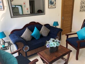 A living room with a blue sofa, two armchairs, a coffee table, and a mirror on the wall.