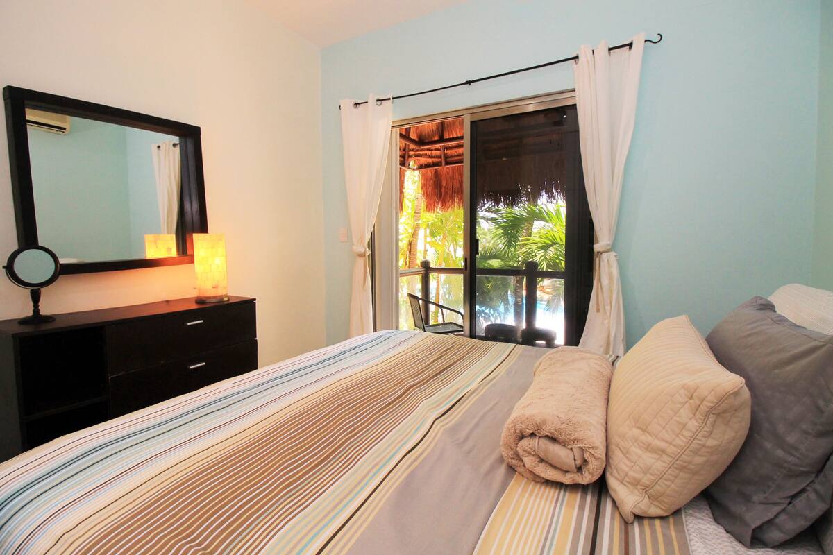 Une chambre à coucher avec un lit, un miroir, une commode et une fenêtre avec des rideaux.