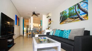 A modern living room with a dark sofa, a glass coffee table, and a painting of a beach scene. - Les Alizes near Beach (Playa del Carmen)