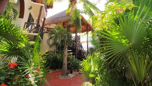 A courtyard with a thatched-roof structure, surrounded by lush greenery and a red pathway. - Les Alizes near Beach (Playa del Carmen)