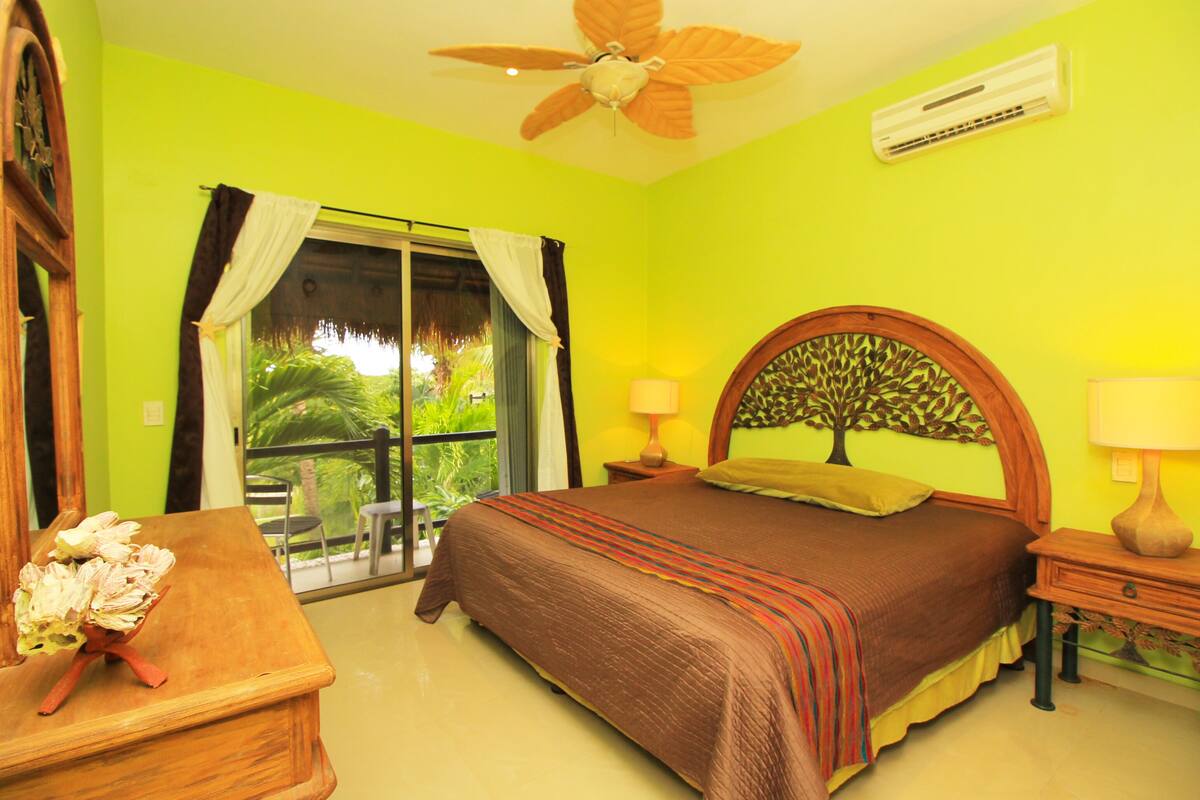 Une chambre avec un lit, une table de chevet en bois, un ventilateur de plafond et une fenêtre avec des rideaux.