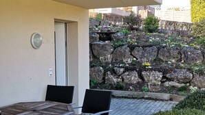 Un patio exterior con mesa y sillas, un muro de piedra con plantas y una puerta.