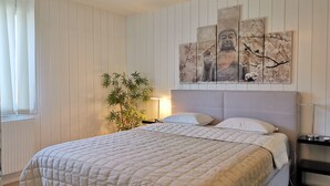 Un dormitorio con una cama, una obra de arte grande en la pared, una planta en maceta y una mesita de noche.