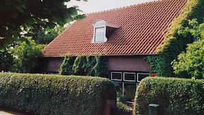Ein Haus mit rotem Ziegeldach, einem kleinen Gaubfenster und einer mit Efeu bewachsenen Ziegelwand.